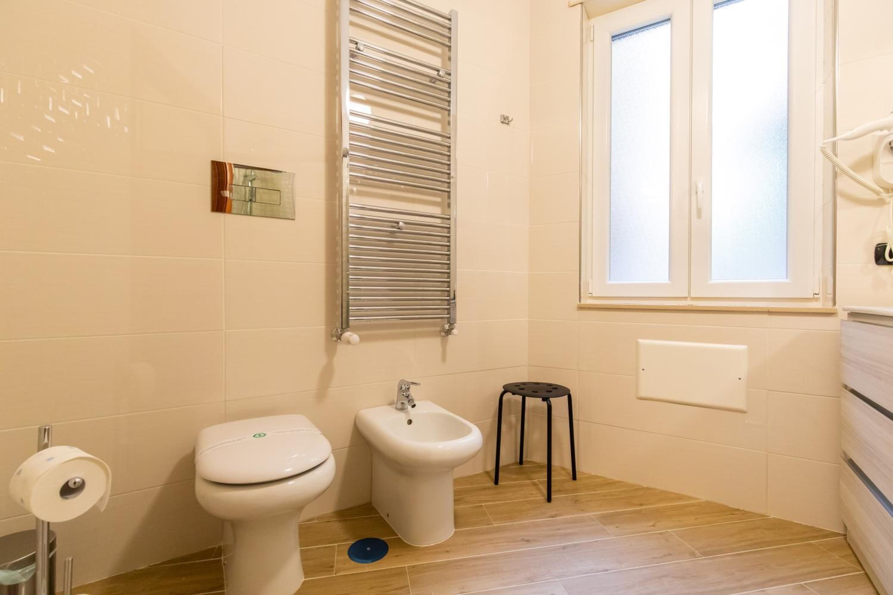 Un baño con inodoro, bidé, toallero y una ventana.