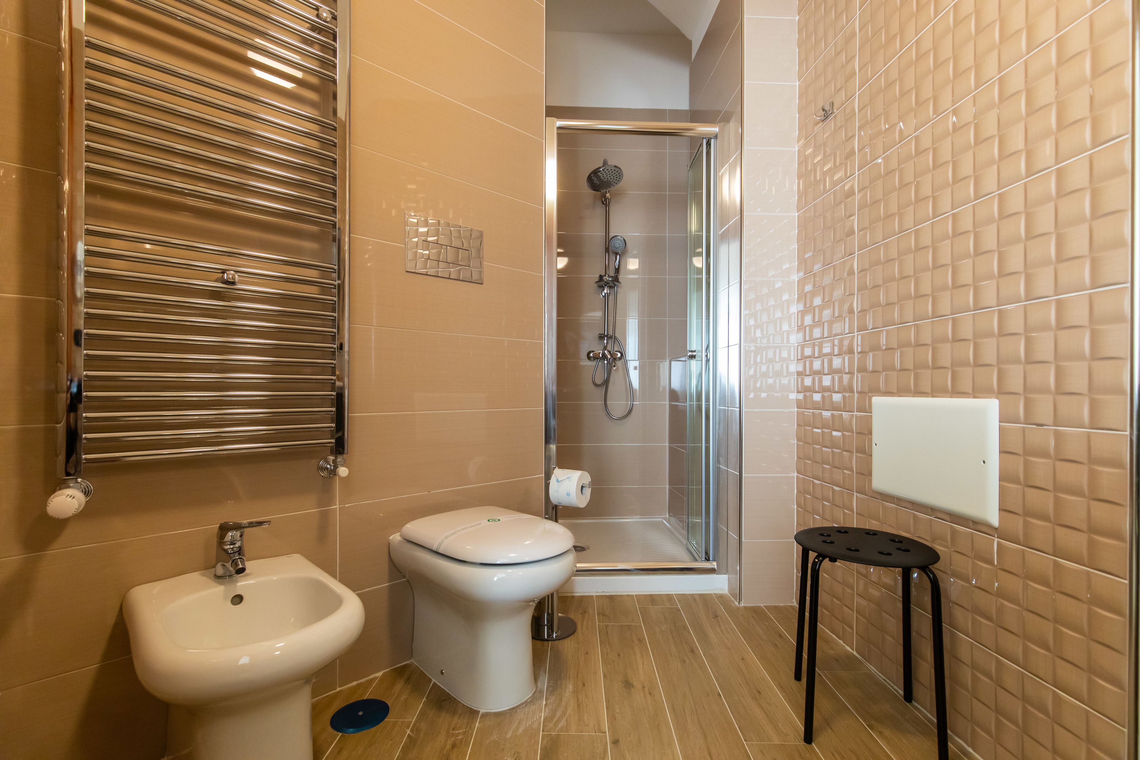 Une salle de bain équipée d’un bidet, de toilettes, d’une douche et d’un petit tabouret.