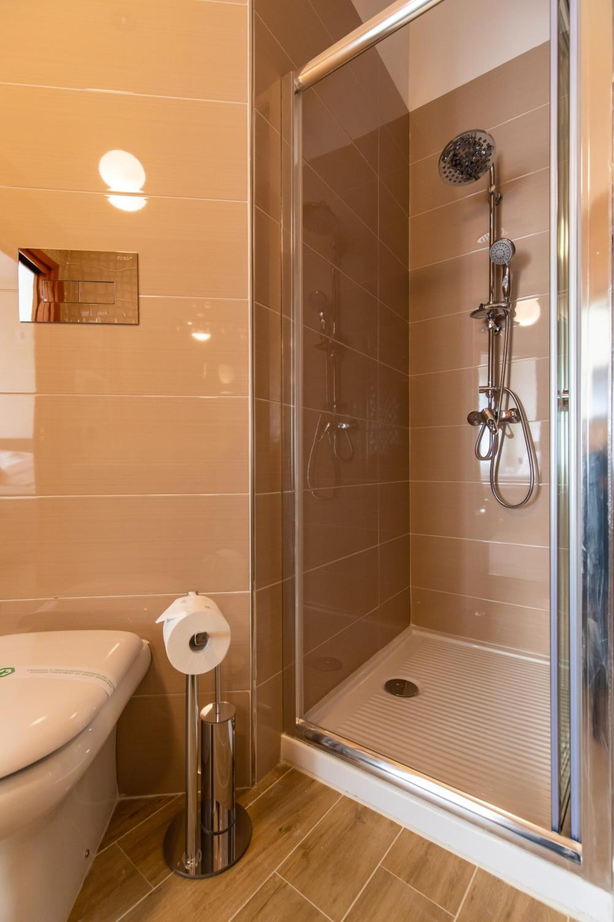 Un baño moderno con ducha envuelta en vidrio, inodoro y dispensador de toallas de papel.