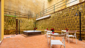 Un patio con paredes de piedra, un jacuzzi, sillas blancas y una mesa.