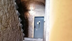 Una escalera conduce a una puerta, con una lámpara colgante encima, en un edificio de paredes rugosas y con textura.