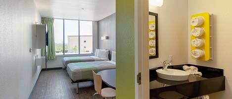 A hotel room with a bed, a desk, and a bathroom with a sink and towel rack.