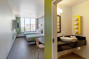 A hotel room with a bed, a desk, and a bathroom with a sink and towel rack. - Motel 6 Austin, TX - Airport (Austin)