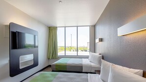 A hotel room with a large window, a flat-screen TV mounted on the wall, a bed with white bedding, and a green and white striped area rug. - Motel 6 Austin, TX - Airport (Austin)