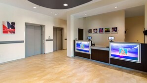 A reception area with a modern design, featuring a reception desk, a digital display, and a ceiling with recessed lighting. - Motel 6 Austin, TX - Airport (Austin)