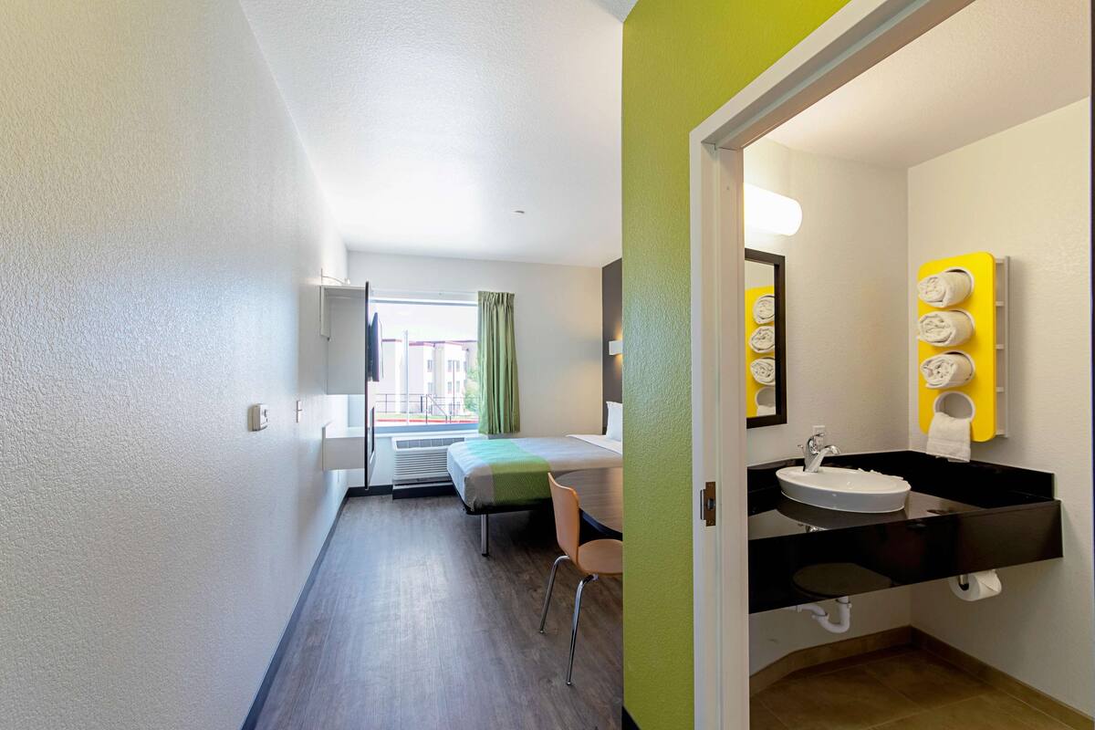 Camera d'albergo con un letto, una sedia, bagno con lavandino e specchio, e vista sull'esterno.