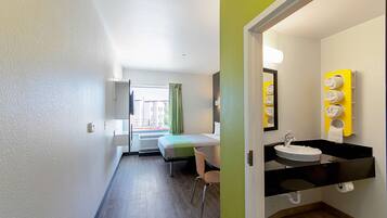 Hotelkamer met een bed, een stoel, een badkamer met wastafel en spiegel, en uitzicht op het omliggende gebied.