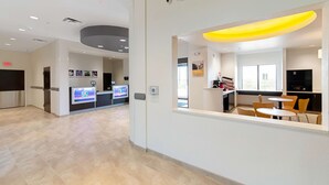 A modern hotel lobby with a reception desk, digital display, seating area, and a view of the dining space. - Motel 6 Austin, TX - Airport (Austin)