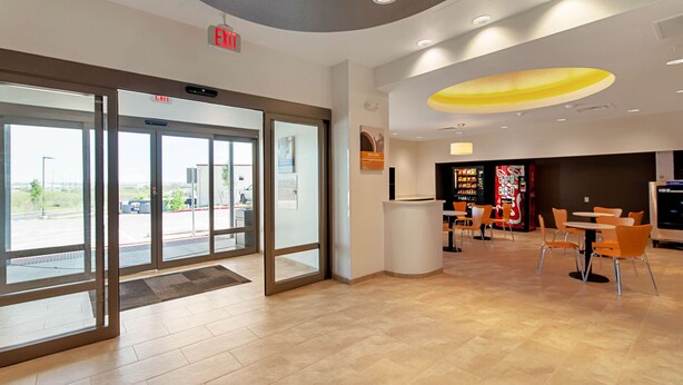 A modern interior with a glass door entrance, a seating area with tables and chairs, and a vending machine. - Studio 6 Austin, TX - Airport (Austin)