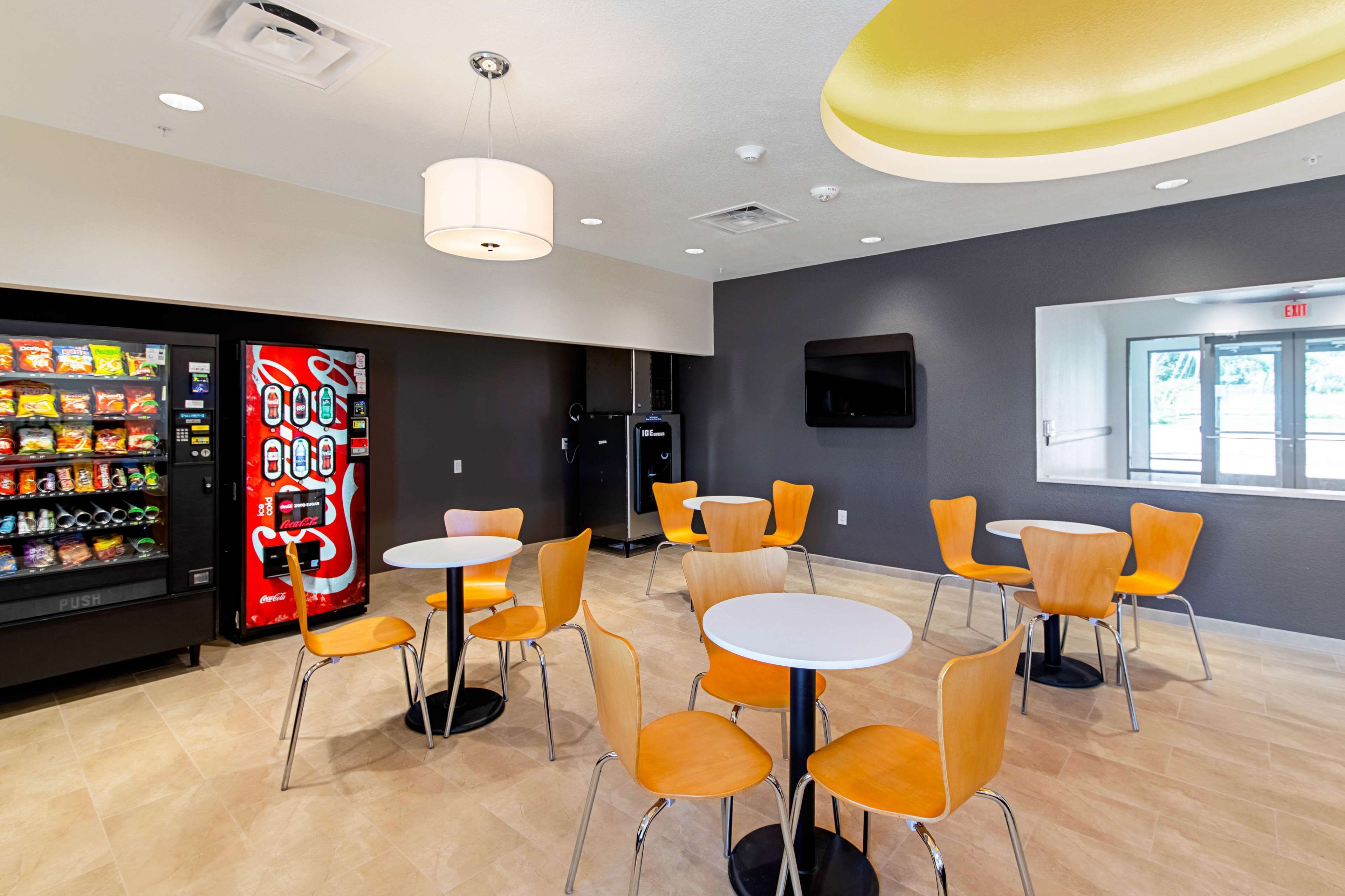 Un comedor moderno con máquinas expendedoras, mesas redondas y sillas color naranja.
