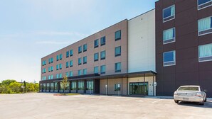 A modern hotel building with a parking lot and a car parked in front. - Studio 6 Austin, TX - Airport (Austin)