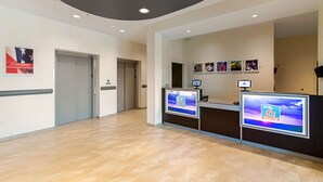 A reception area with a modern design, featuring a reception desk, a digital display, and a ceiling with recessed lighting. - Studio 6 Austin, TX - Airport (Austin)