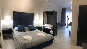 A modern hotel room with a large bed, bedside tables, a wardrobe, and a seating area with a sofa and chairs. - Re di Smirne (Bari)