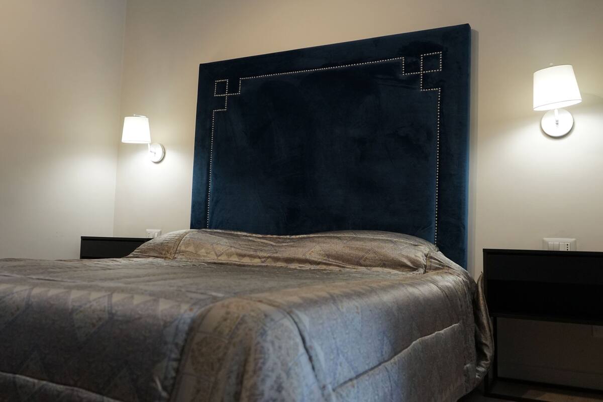 Un lit bien fait, avec une tête de lit sombre et deux lampes de chevet.