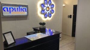 A reception desk with a sign reading "apulia ACCOMMODATION.IT", a decorative light fixture, and a framed map on the desk. - Re di Smirne (Bari)