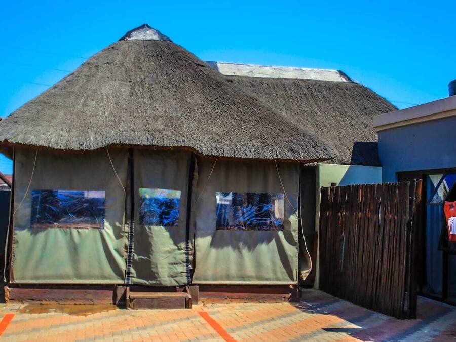 Una estructura de techo de paja con ventanas, una valla de madera y un área pavimentada.