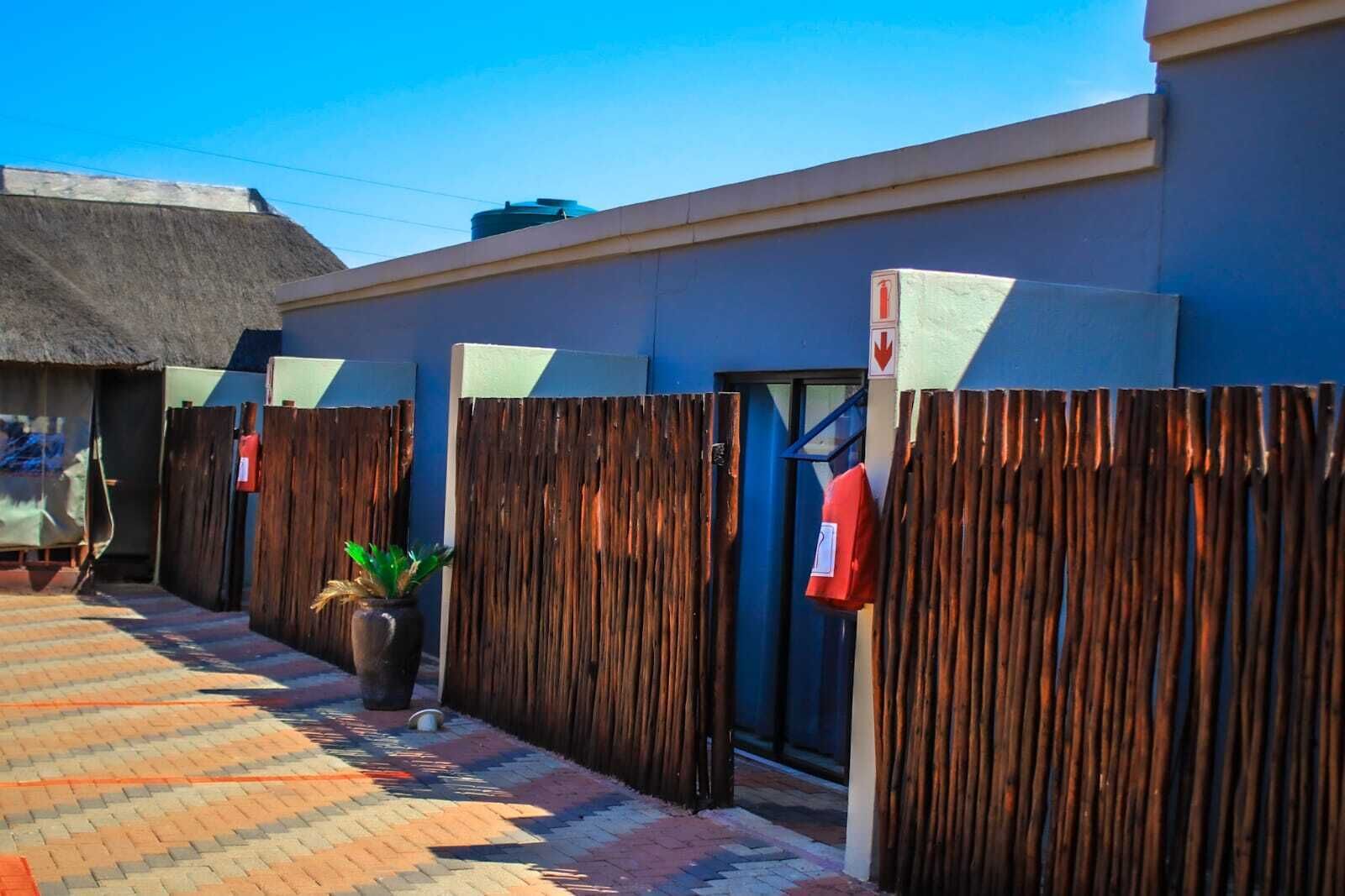 A building with a blue exterior, a wooden fence, and a thatched-roof structure in the background.