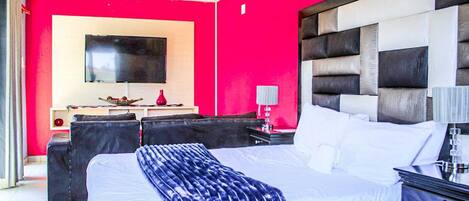 Habitación de hotel con una cama grande, un televisor de pantalla plana en la pared, un escritorio con lámpara y una pared de acento en rojo.