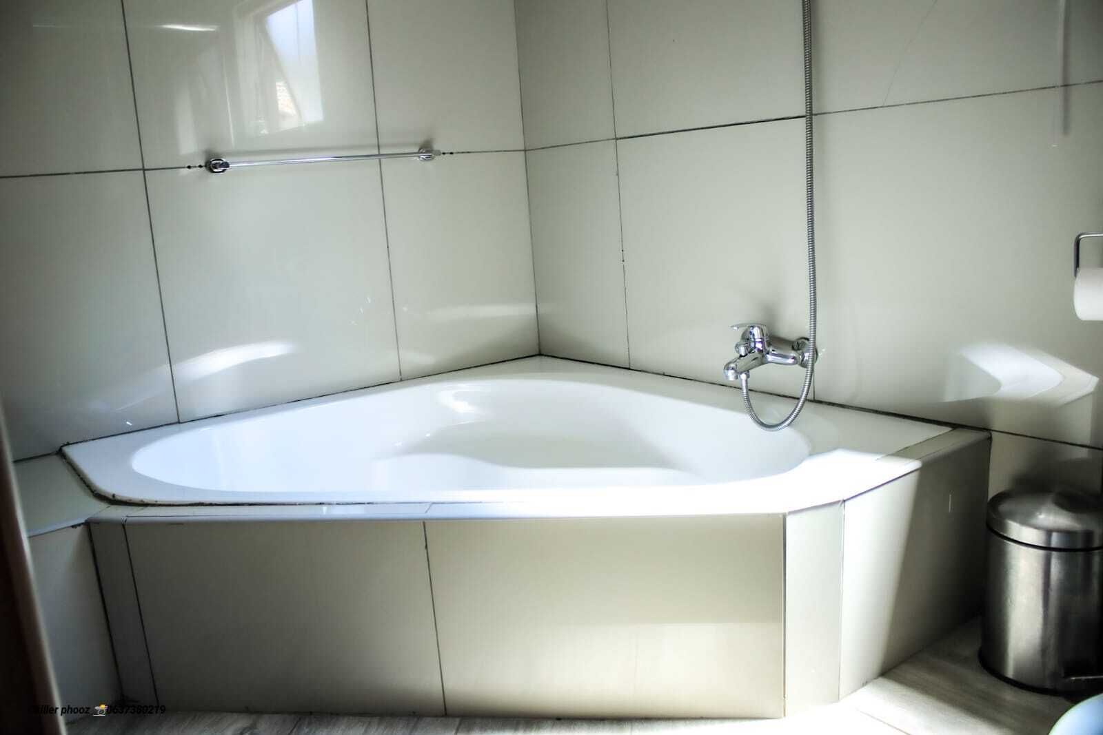 Een hoekbadkamer met een vrijstaand bad, een douchekop en een prullenbak.