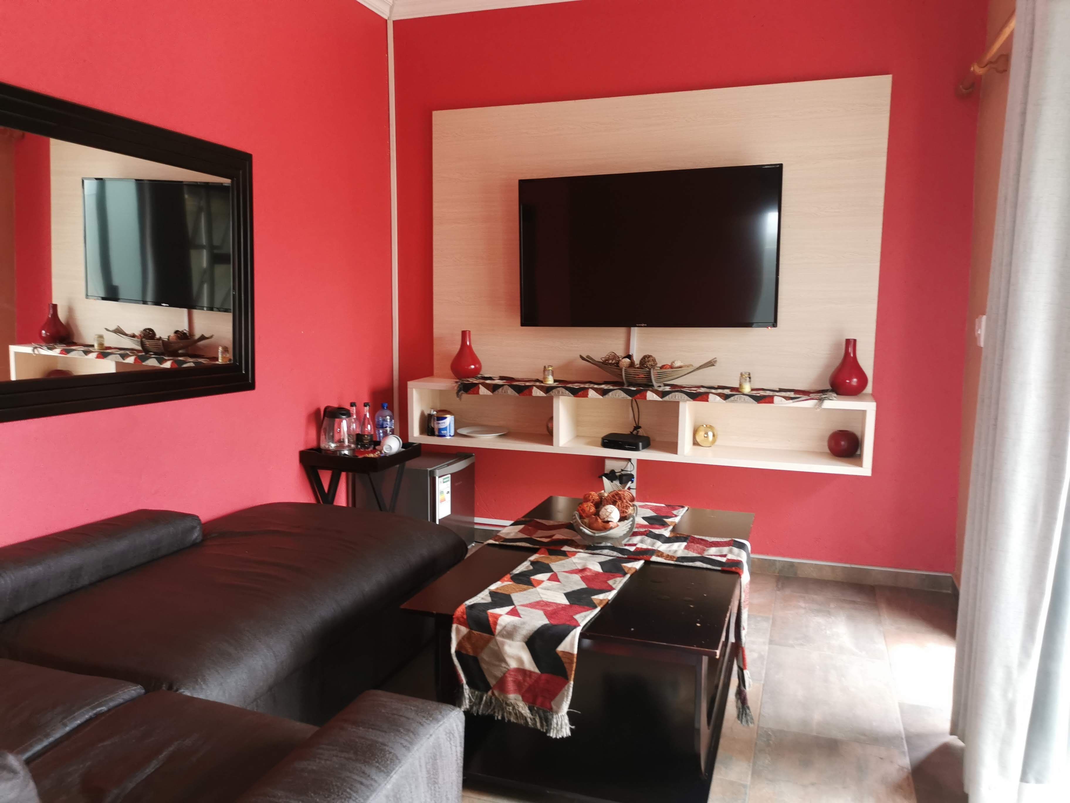 A living room with a sofa, a coffee table, a TV mounted on the wall, and a small shelf with decorative items.