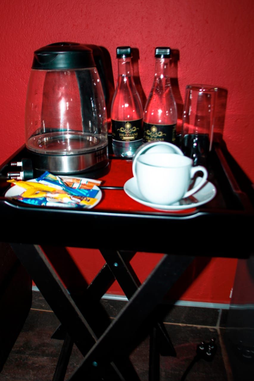 A tray with a coffee maker, two bottles of tea, a cup, and a plate with snacks.