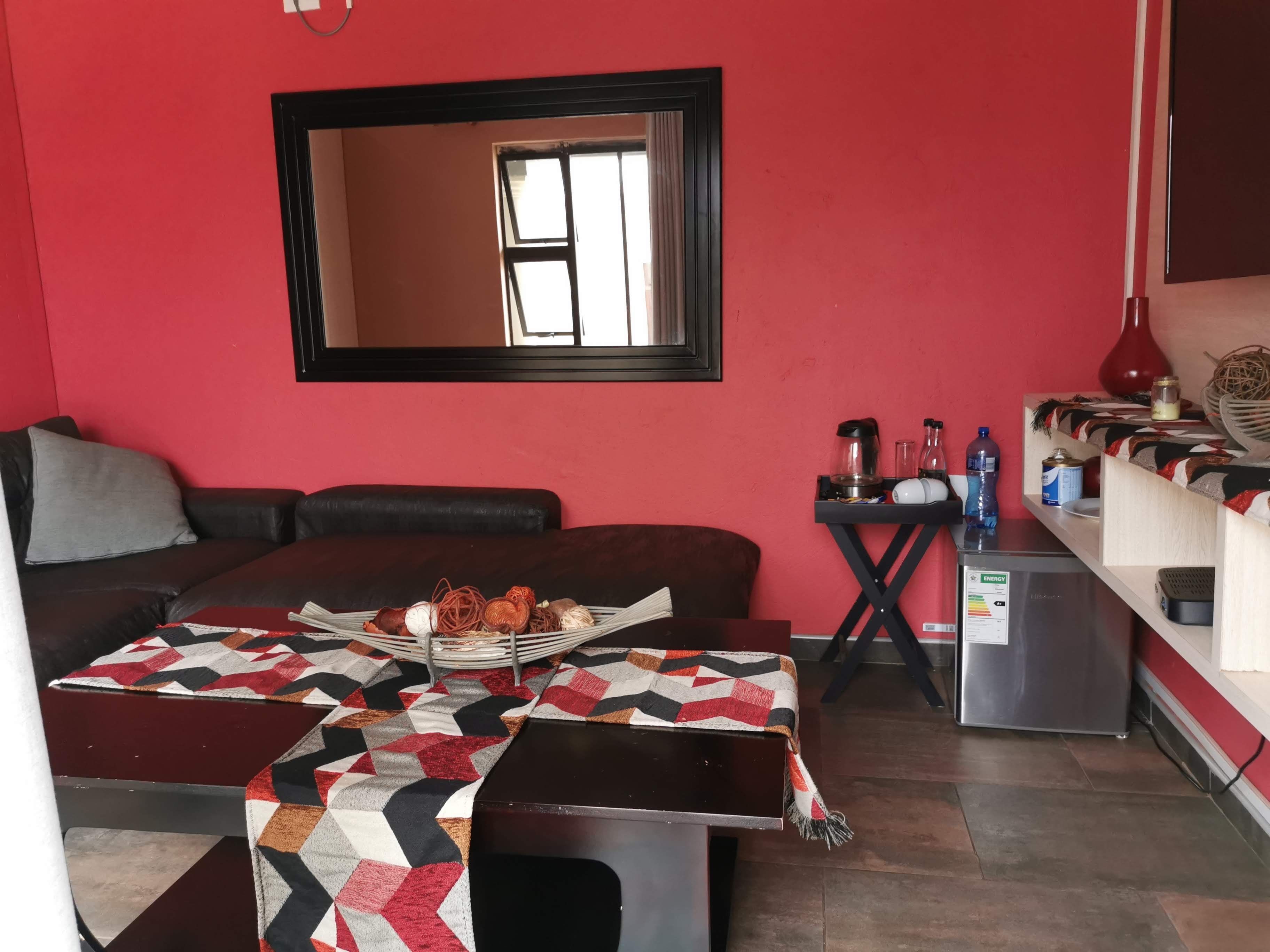 Un espacio habitable compacto con un sofá, una mesita con mantel estampado, una cafetera y un refrigerador.
