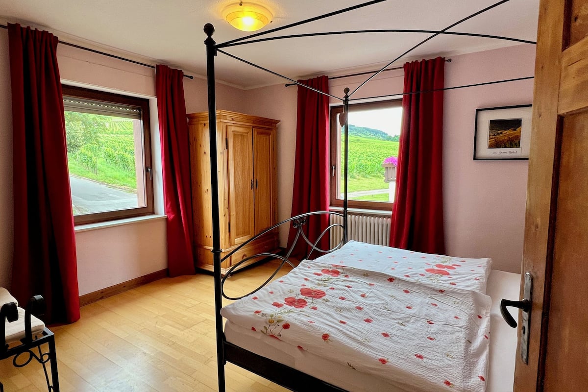 Quarto com cama de dossel, guarda-roupa de madeira e janela com vista para o verde.