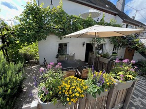 An outdoor patio area with a table and chairs, surrounded by potted plants and a wooden fence. - Ferienweingut Matthias Löwen (Detzem)