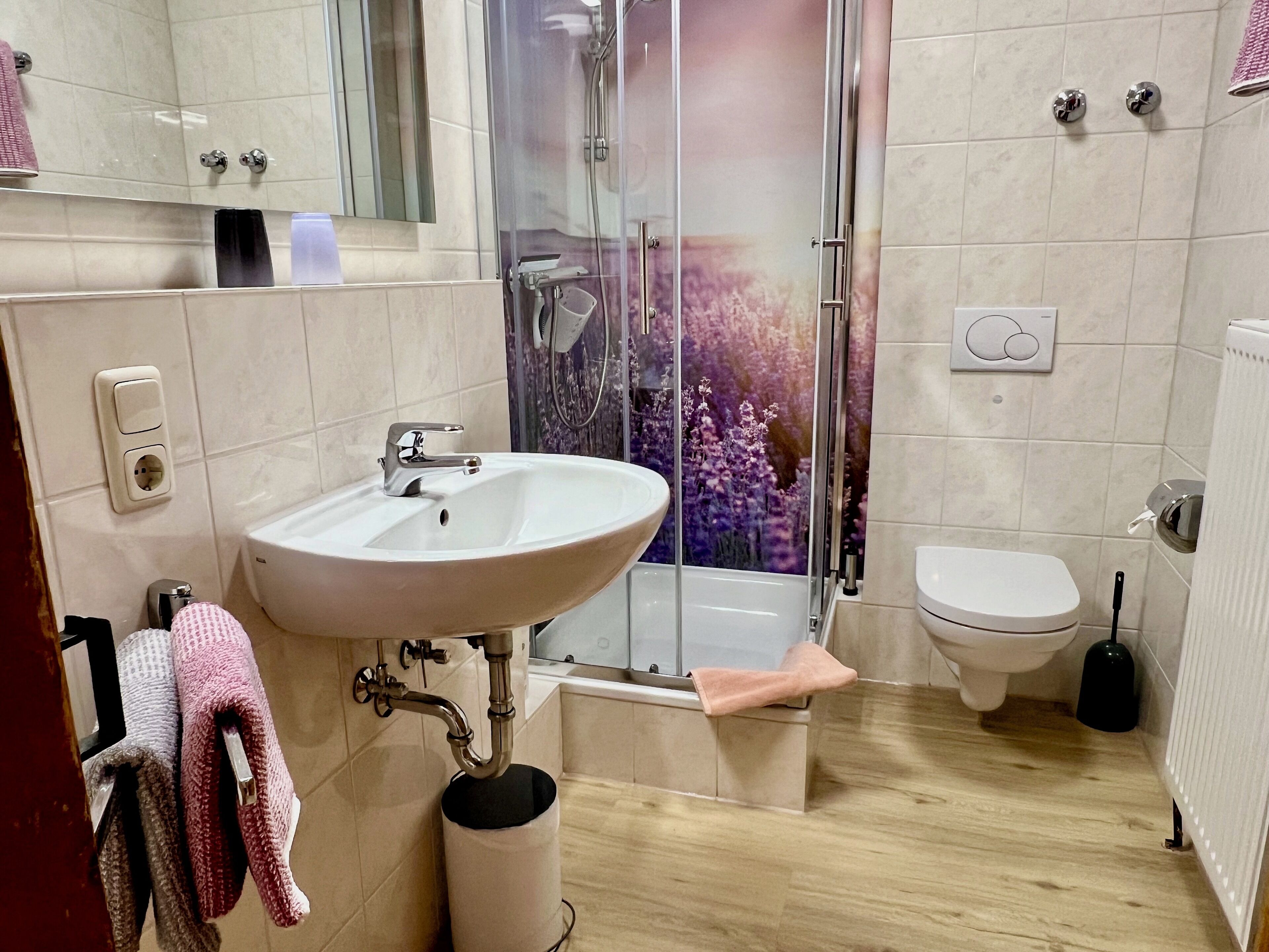 A modern bathroom with a white sink, a glass-enclosed shower, a toilet, and a towel rack with multiple towels.