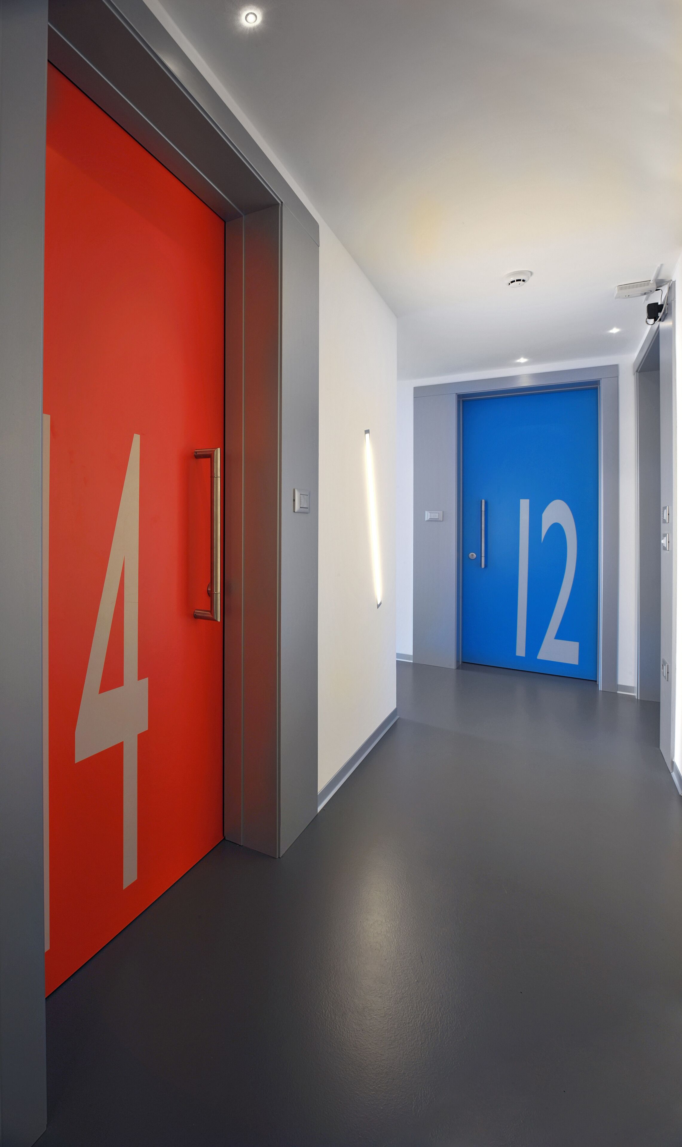 Un pasillo moderno con una puerta roja con el número 4 y una puerta azul con el número 12.