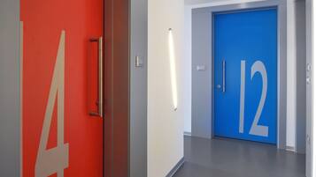 Un pasillo moderno con una puerta roja con el número 4 y una puerta azul con el número 12.