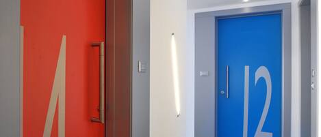 Un couloir moderne avec une porte rouge portant le numéro « 4 » et une porte bleue portant le numéro « 12 ».