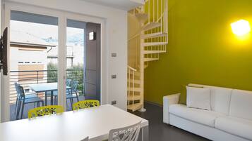 Un interior moderno con una mesa y sillas de comedor blancas, un sofá blanco, una pared de acento amarilla y una escalera de caracol.