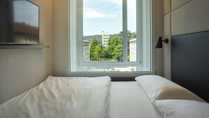 Un dormitorio moderno con un ventanal grande, una cama, una mesita de noche y una lámpara colgante.