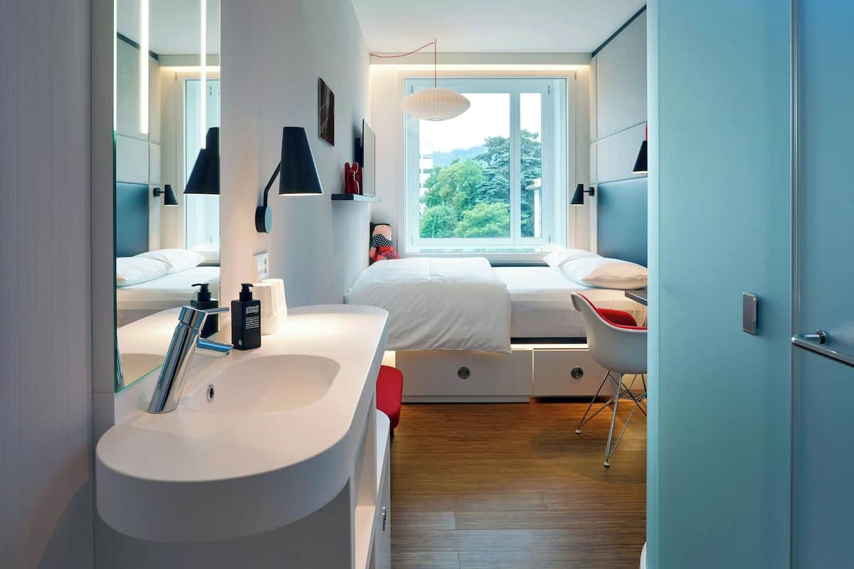 Une chambre moderne avec une grande fenêtre, un lavabo blanc et une chaise rouge.