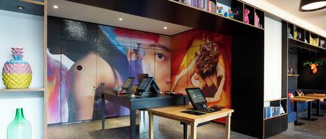 Un interior moderno con una gran pantalla de arte digital, una recepción con una computadora portátil y una estantería con diversos objetos.