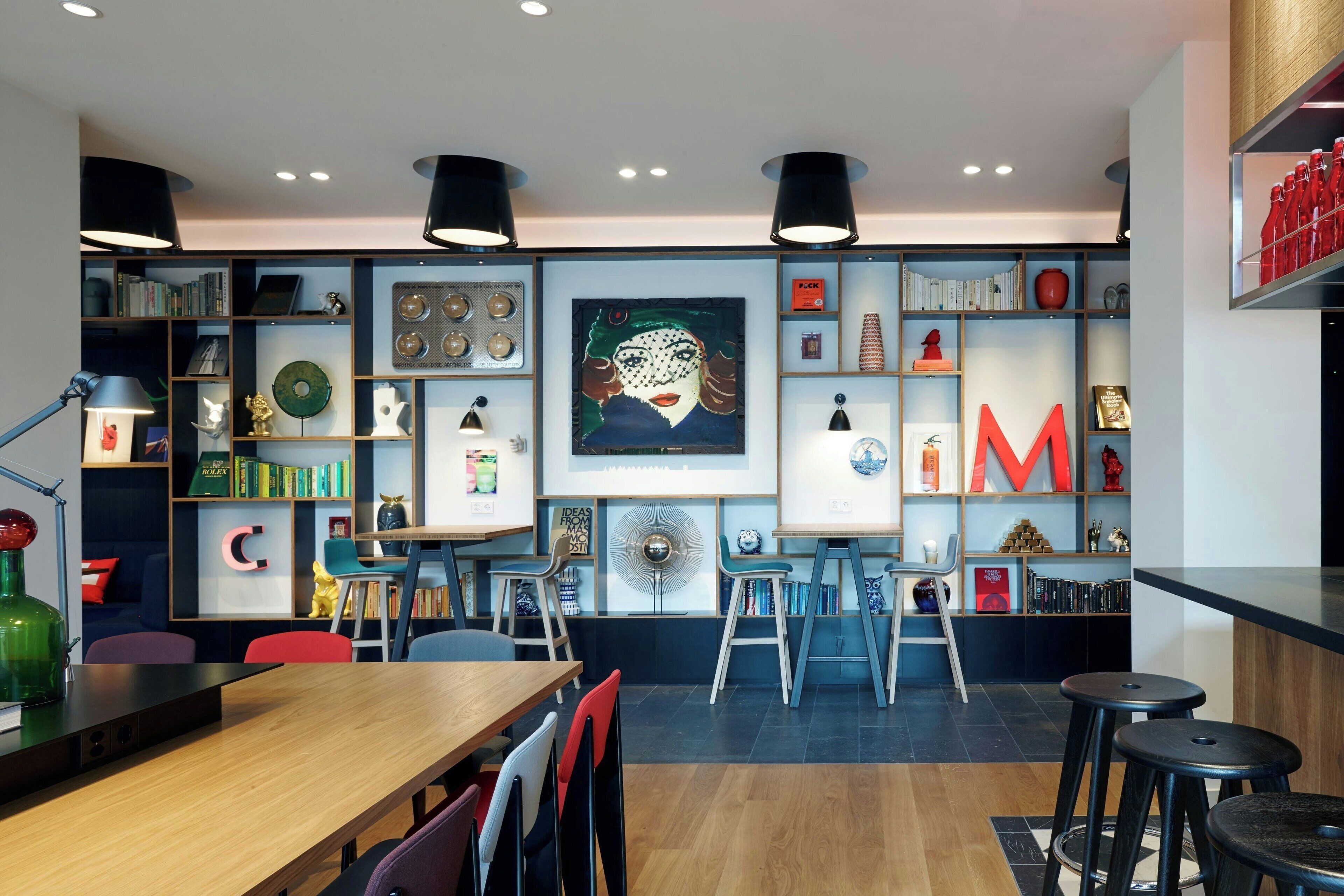 A modern interior with a wooden table, bar stools, a bookshelf, and a large framed artwork.