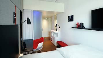 Ein modernes Hotelzimmer mit Bett, Schreibtisch, Stuhl, Schminktisch und Fernseher an der Wand.
