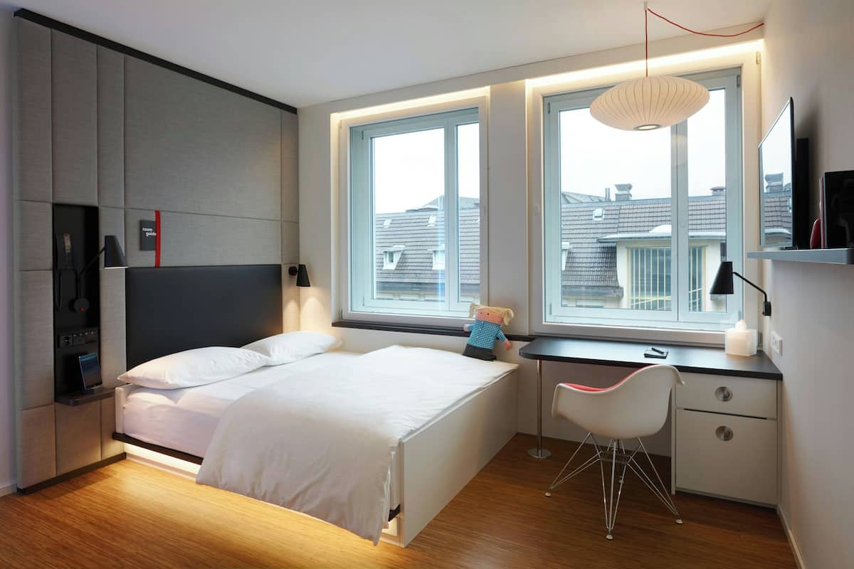Une chambre moderne avec un lit, un bureau, une chaise et de grandes fenêtres.