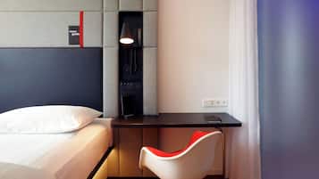 A hotel room with a bed, a desk with a lamp, a chair, and a small table.