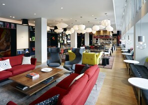 A modern lounge area with red sofas, a wooden coffee table, and a variety of seating options including armchairs and a bench.