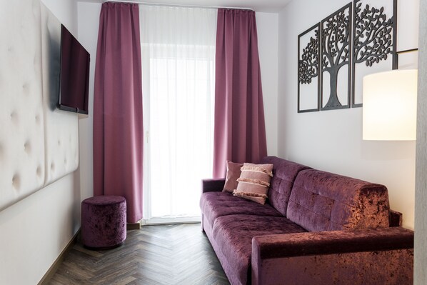 Una sala de estar moderna con un sofá, un otoman redondos, un televisor de pantalla plana y una obra de arte colgada en la pared.