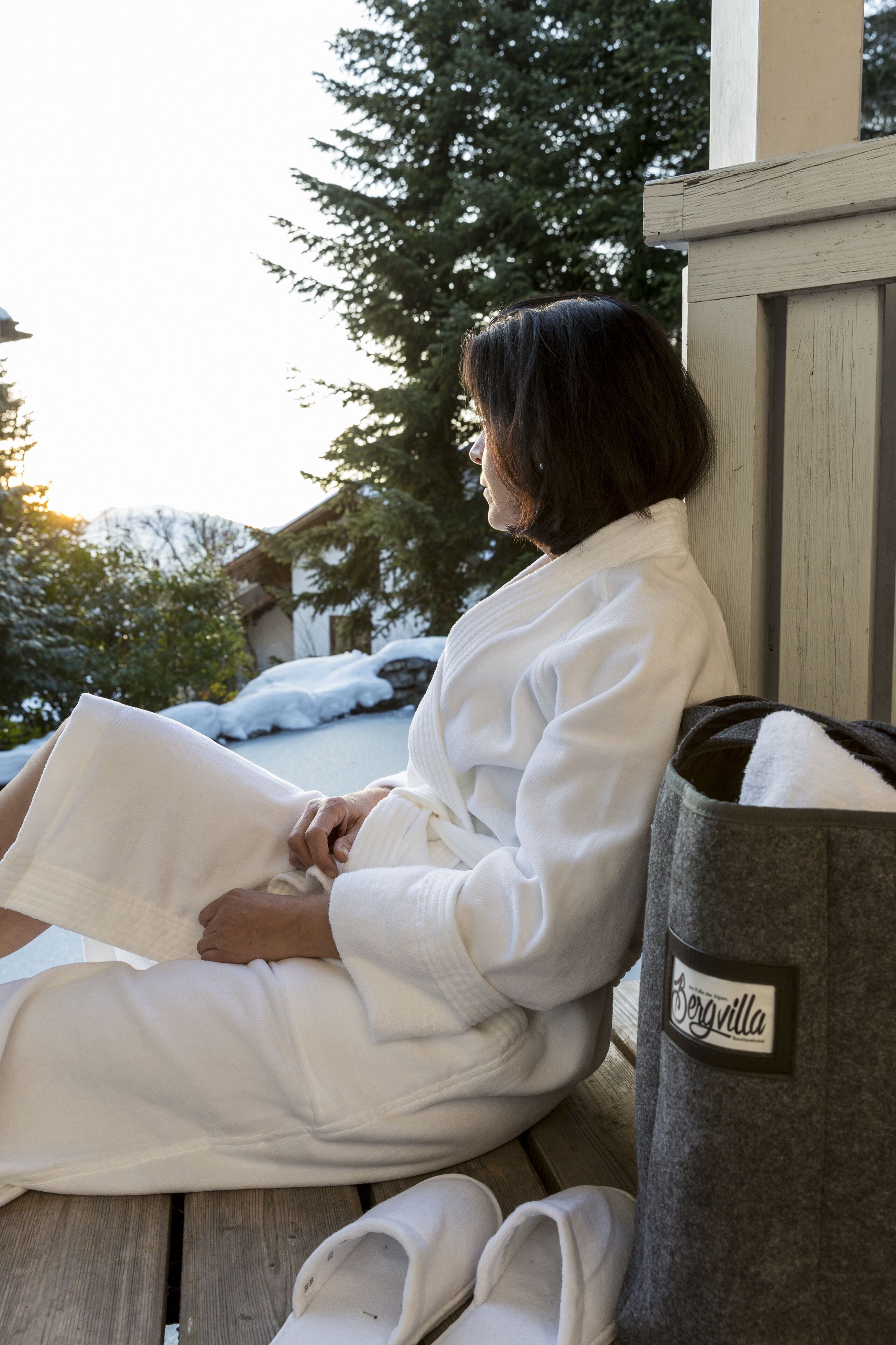 A person sitting on a wooden bench outdoors, reading a book.