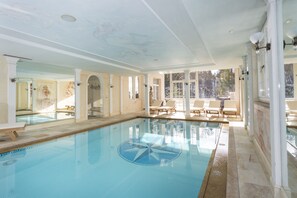 Une grande piscine intérieure dont le fond est décoré d’un motif en forme d’étoile, entourée de chaises longues et d’un grand miroir qui reflète la pièce.