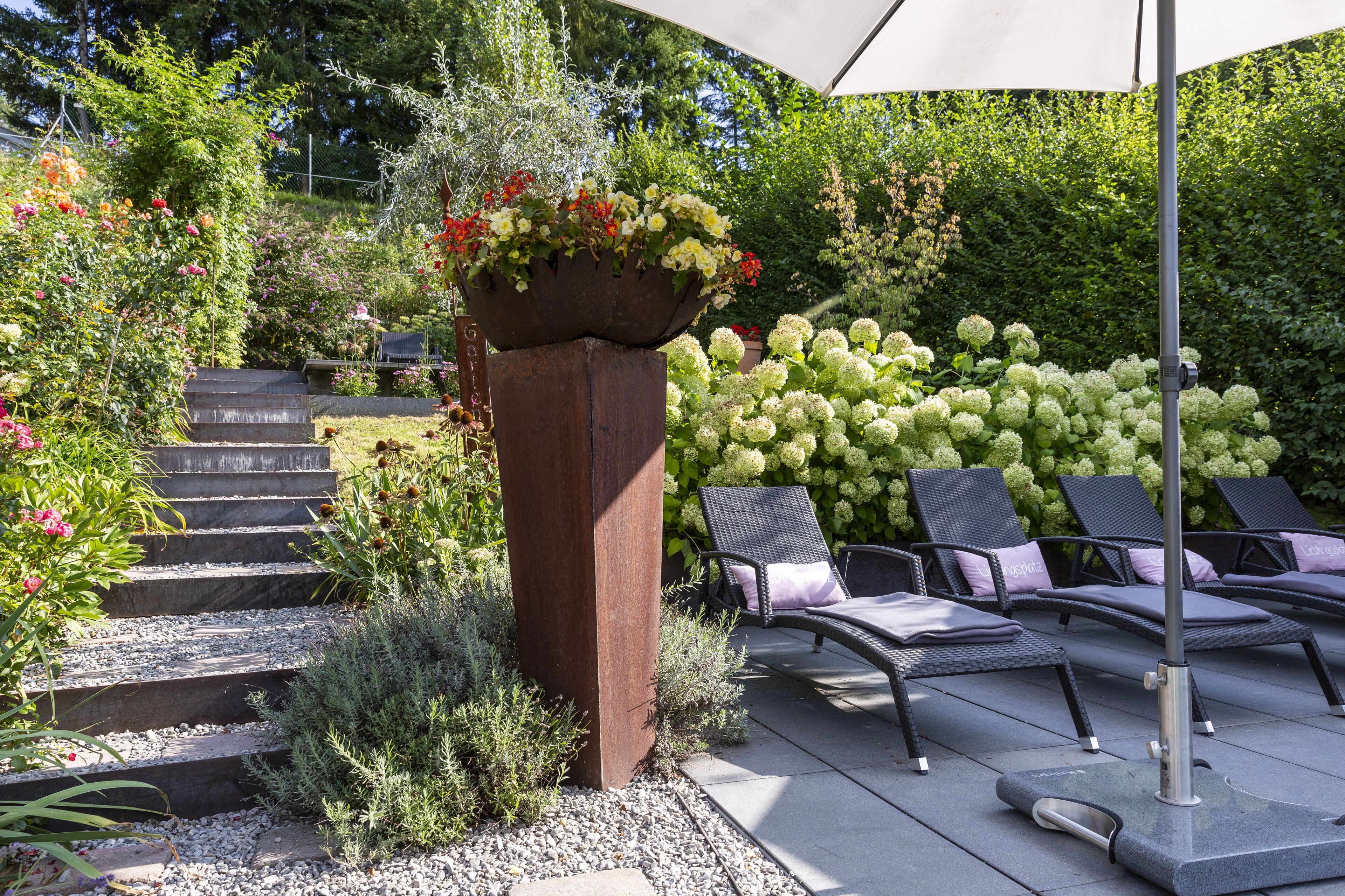 Un patio con mobiliario exterior, una jardinera con flores y un seto.