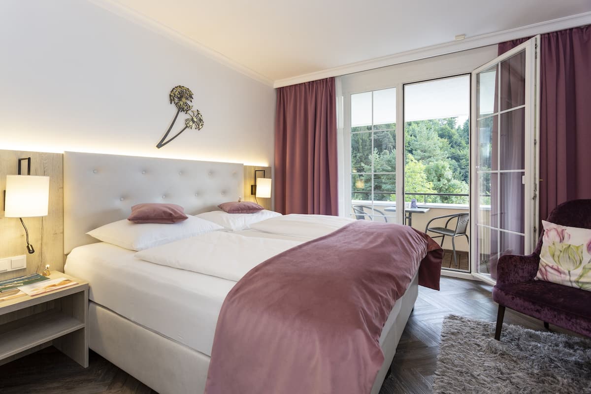 A bedroom with a large bed, a nightstand, a chair, and a view of the outdoors through a sliding glass door.