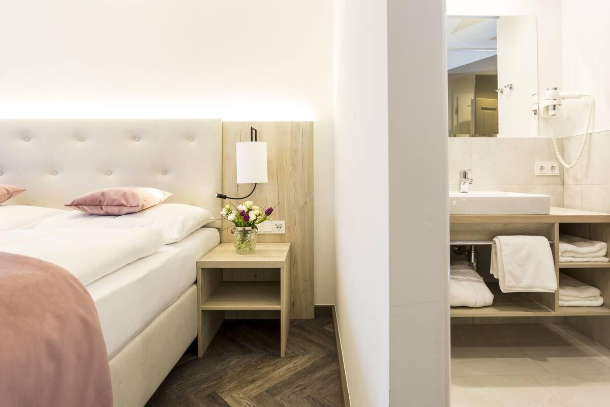 A hotel room with a bed, bedside table with a lamp, a small shelf, and a mirror.