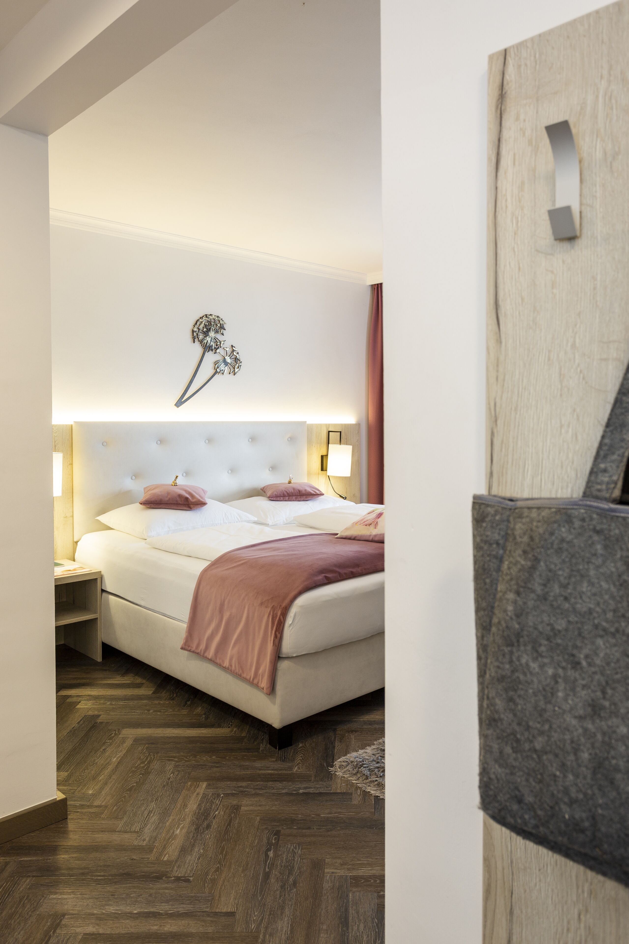A modern bedroom with a large bed, bedside lamps, and a decorative wall piece.
