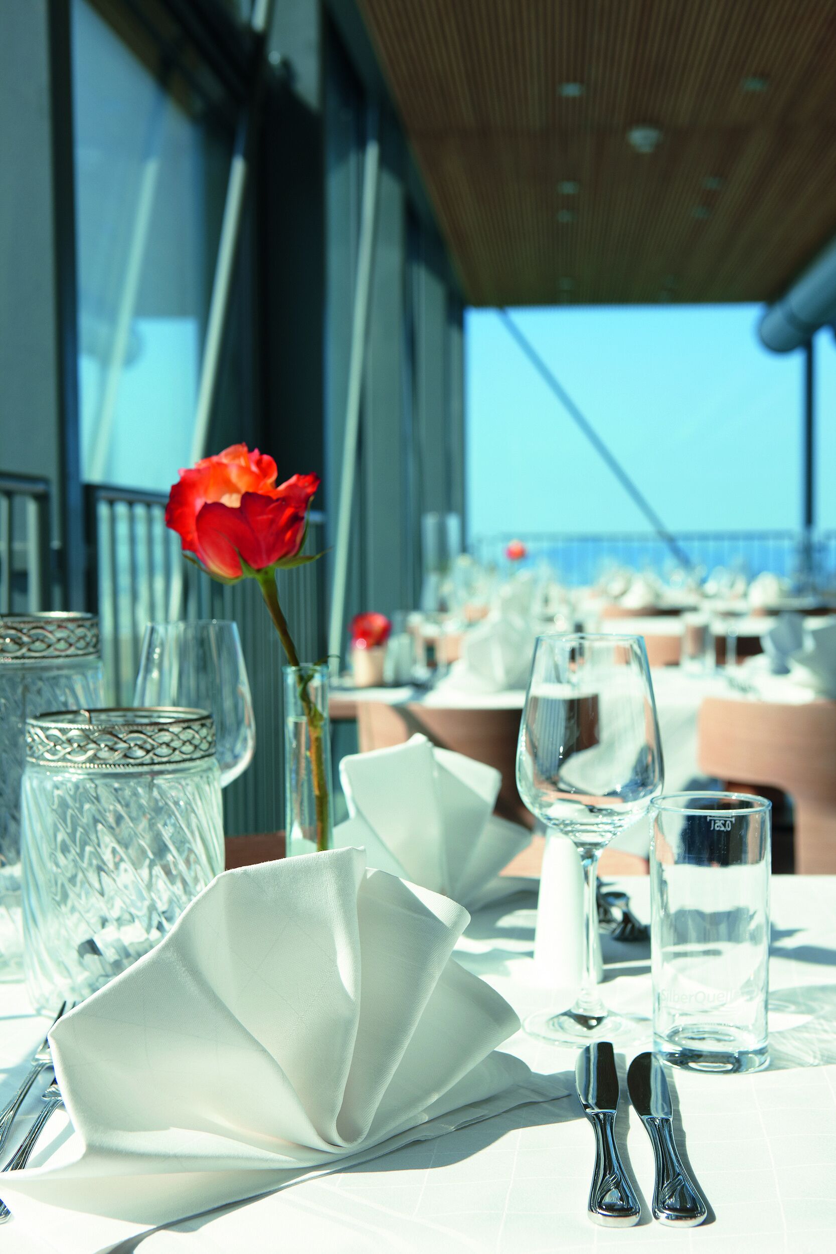 A table set for dining with a rose in a vase, clear glasses, and cutlery.