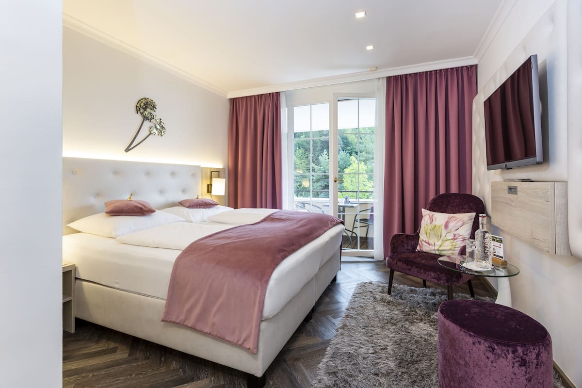 A modern bedroom with a large bed, a glass coffee table, a purple armchair, and a TV mounted on the wall.